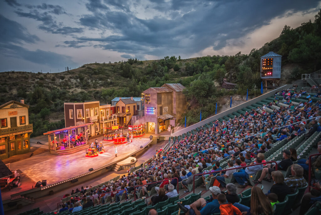 A full crowd watches the Medora Musical, in Medora ND, with a dramatic sunset and North Dakota Badlands in the background.