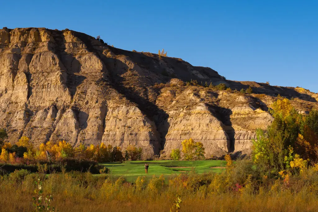 A golfer stands on a green at Bully Pulpit Golf Course in Medora, ND. He is dwarfed by the buttes and fall foliage surrounding the course.