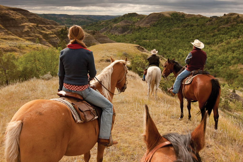 Trail Rides in Medora, ND. Three riders on horses look out over the dramatically lit Badlands.