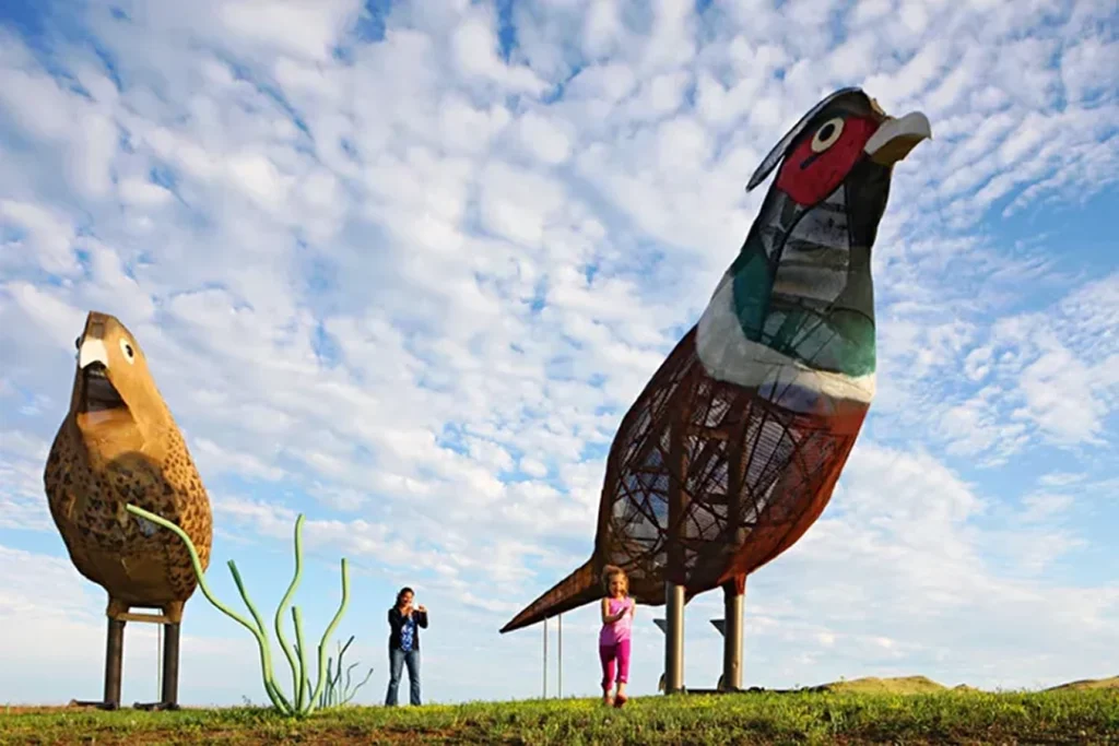 A woman takes a photo as a child runs between two giant metal bird sculptures along the Enchanted Highway, a popular roadtrip destination in North Dakota