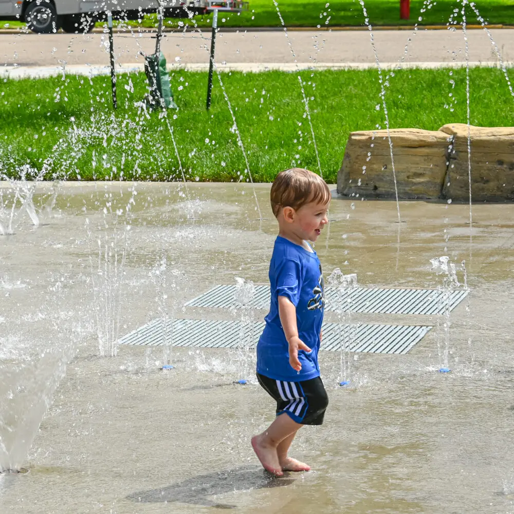 little boy running through sprinkler water
