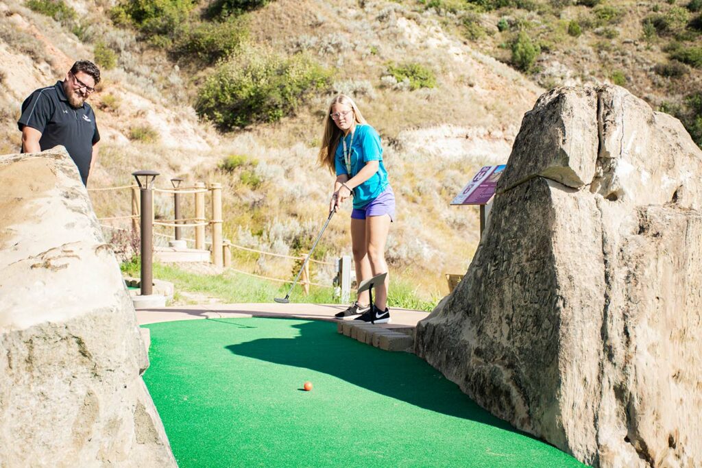 Girl watches her golf ball roll down a ling mini golf green after putting.