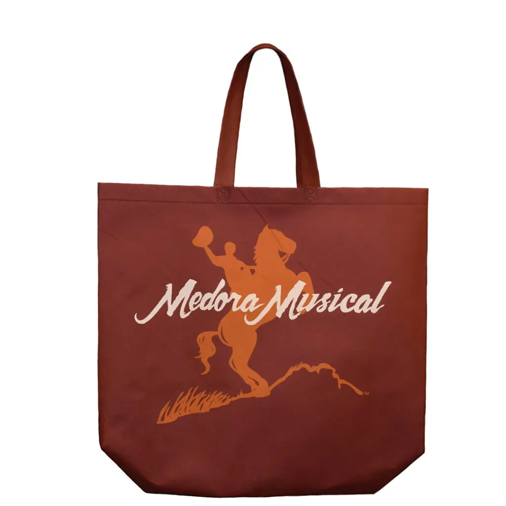 A tote bag with a graphic of a man riding a horse overlayed with the logo which reads "Medora Musical" which can be found in stores in Medora, North Dakota