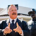 Joe Wiegand stands dressed as Theodore Roosevelt points and talks to visitors in front of a Theodore Roosevelt statue and the Old Town Hall Theater, a historic theater in downtown Medora, North Dakota