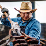 A chef in a cowboy hat holds a pitchfork loaded up in steaks and serves them at the Pitchfork Steak Fondue, a dining attraction in Medora, North Dakota