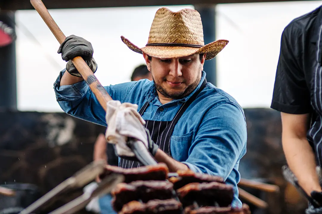 A chef in a cowboy hat holds a pitchfork loaded up in steaks and serves them at the Pitchfork Steak Fondue, a dining attraction in Medora, North Dakota