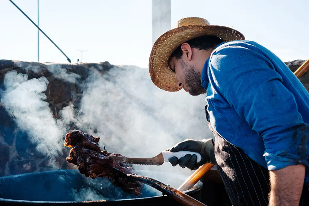 A chef in an apron and cowboy hat stand over a oil vat and checks 12 oz steaks stacked on a pitchfork at the Pitchfork Steak Fondue, a dining attraction in Medora, North Dakota