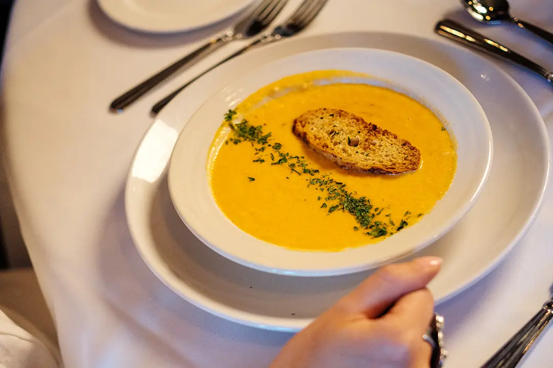 A bowl of lobster bisque soup topped with green herbs and a small slice of bread sits on a table in Theodore's Dining Room, a restaurant in Medora, North Dakota