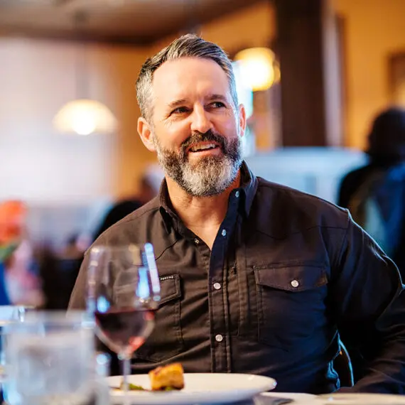 A man sits at a table with a plate of food and glass of wine in Theodore's Dining Room, a high-end restaurant in Medora, North Dakota