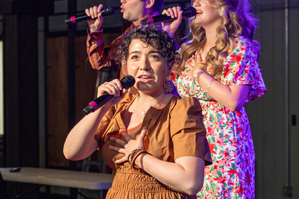 A women in an orange dress with dark curly hair looks into the audience as she sings on stage at the Medora Gospel Brunch, a popular entertainment attraction in Medora, North Dakota