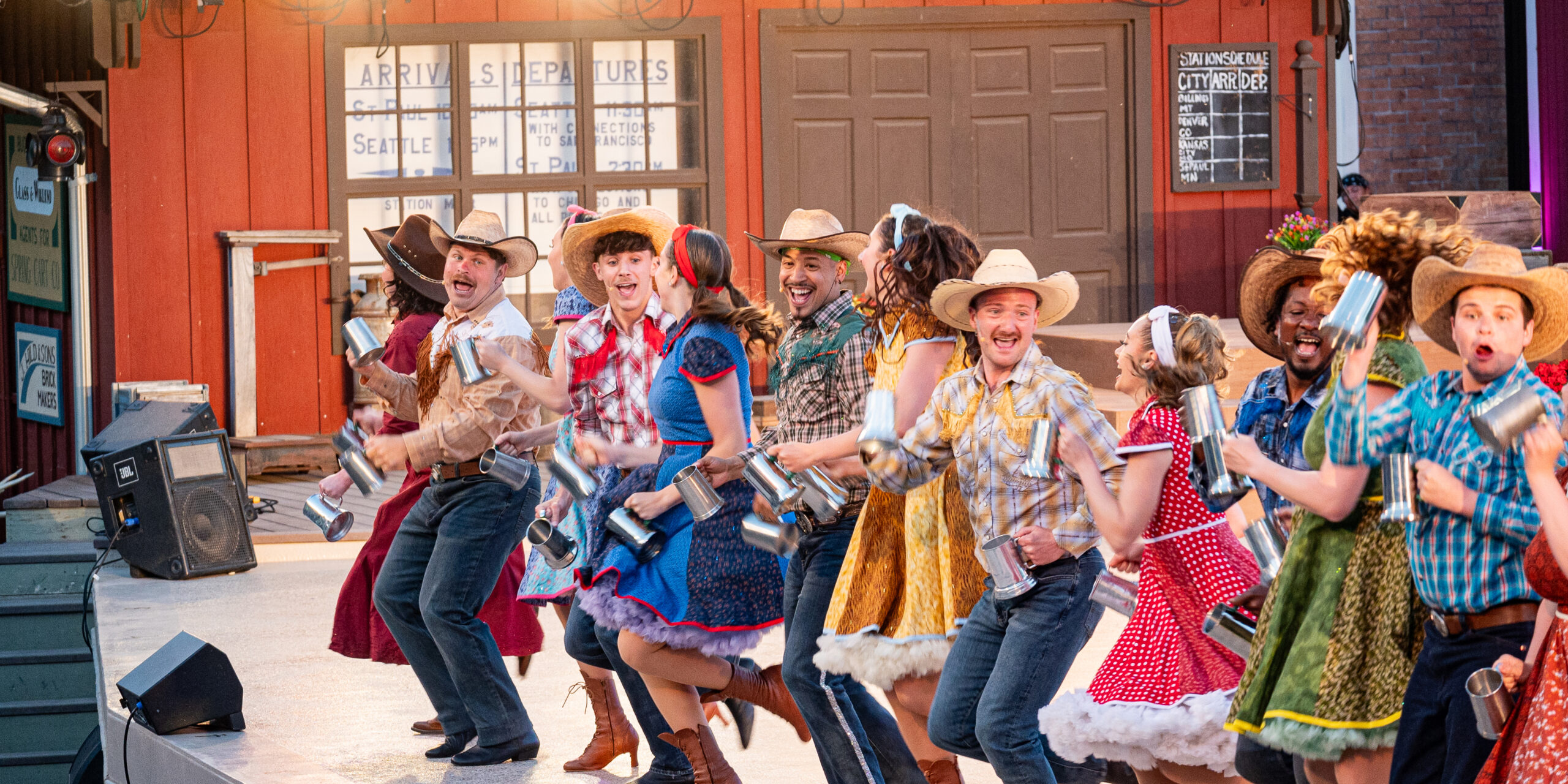 A group of dancers in colorful cowboy costumes dance with mugs on stage at the Medora Musical, a popular entertainment attraction in Medora, North Dakota