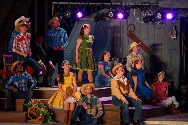 A group of singers in colorful cowboy costumes smiles and sing on stage at the Medora Musical, a popular entertainment attraction in Medora, North Dakota