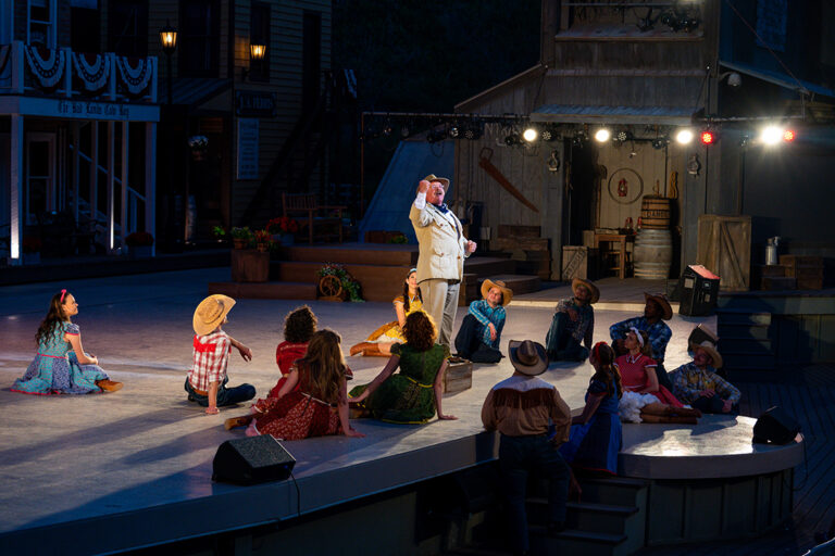 Theodore Roosevelt stands on stage lifting his fist during a speech as other performers sit and watch on stage at the Medora Musical, a popular entertainment attraction in Medora, North Dakota