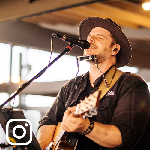 man singing into microphone and playing guitar and harmonica