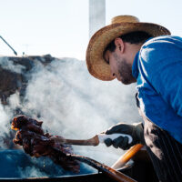 A chef in an apron and cowboy hat stands over an oil vat, checking 12 oz steaks stacked on a pitchfork at the Pitchfork Steak Fondue in Medora, North Dakota.